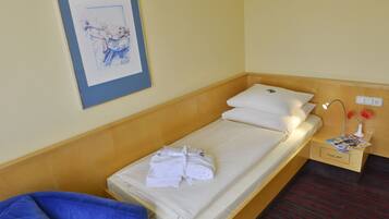 A single bed with white linens, a wooden headboard, a small bedside table with a lamp, and a framed picture on the wall.