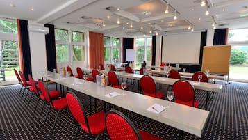 A conference room with a long table, red chairs, and a projector screen.