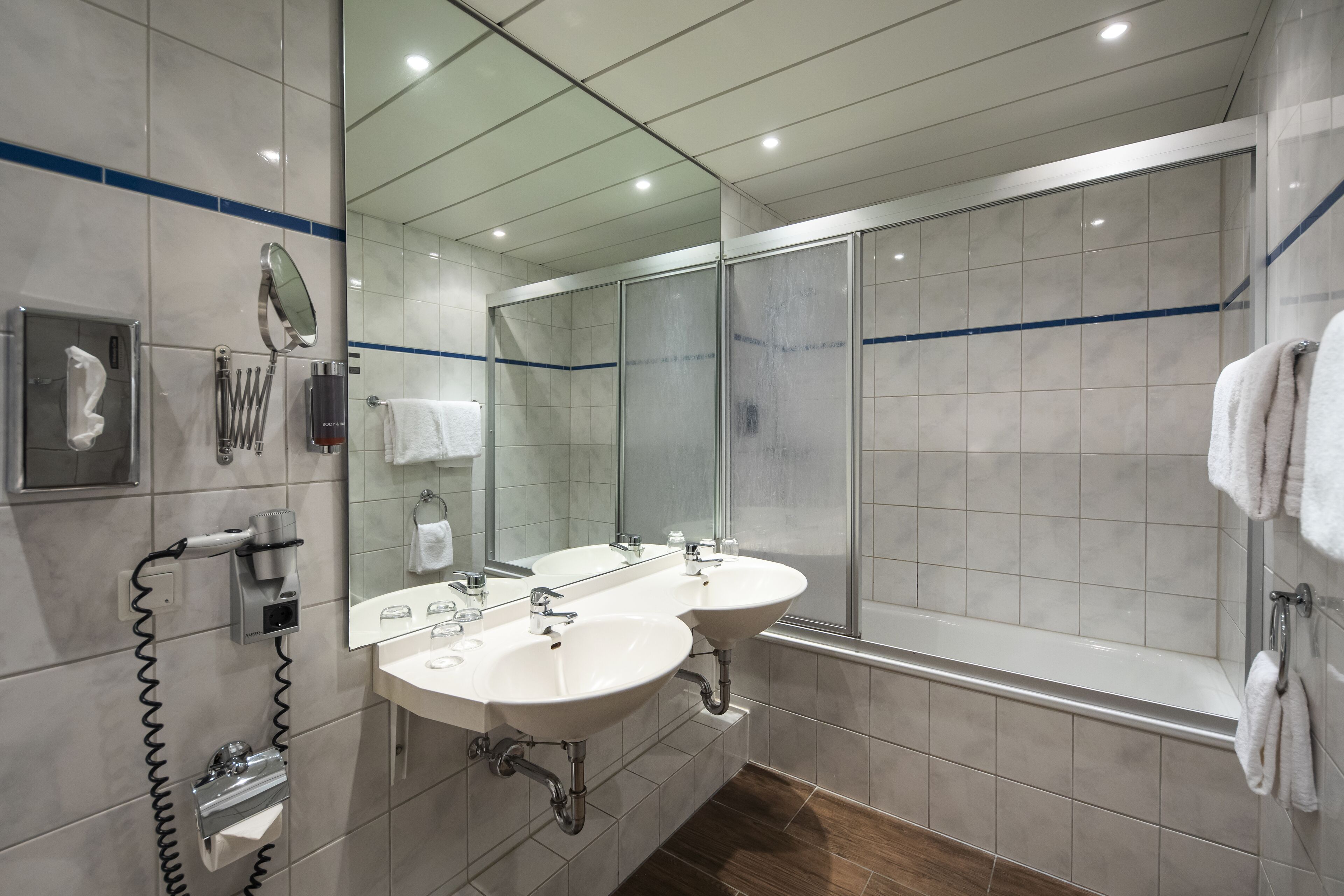 A modern bathroom with two sinks, a large mirror, a hairdryer, and a shower area.