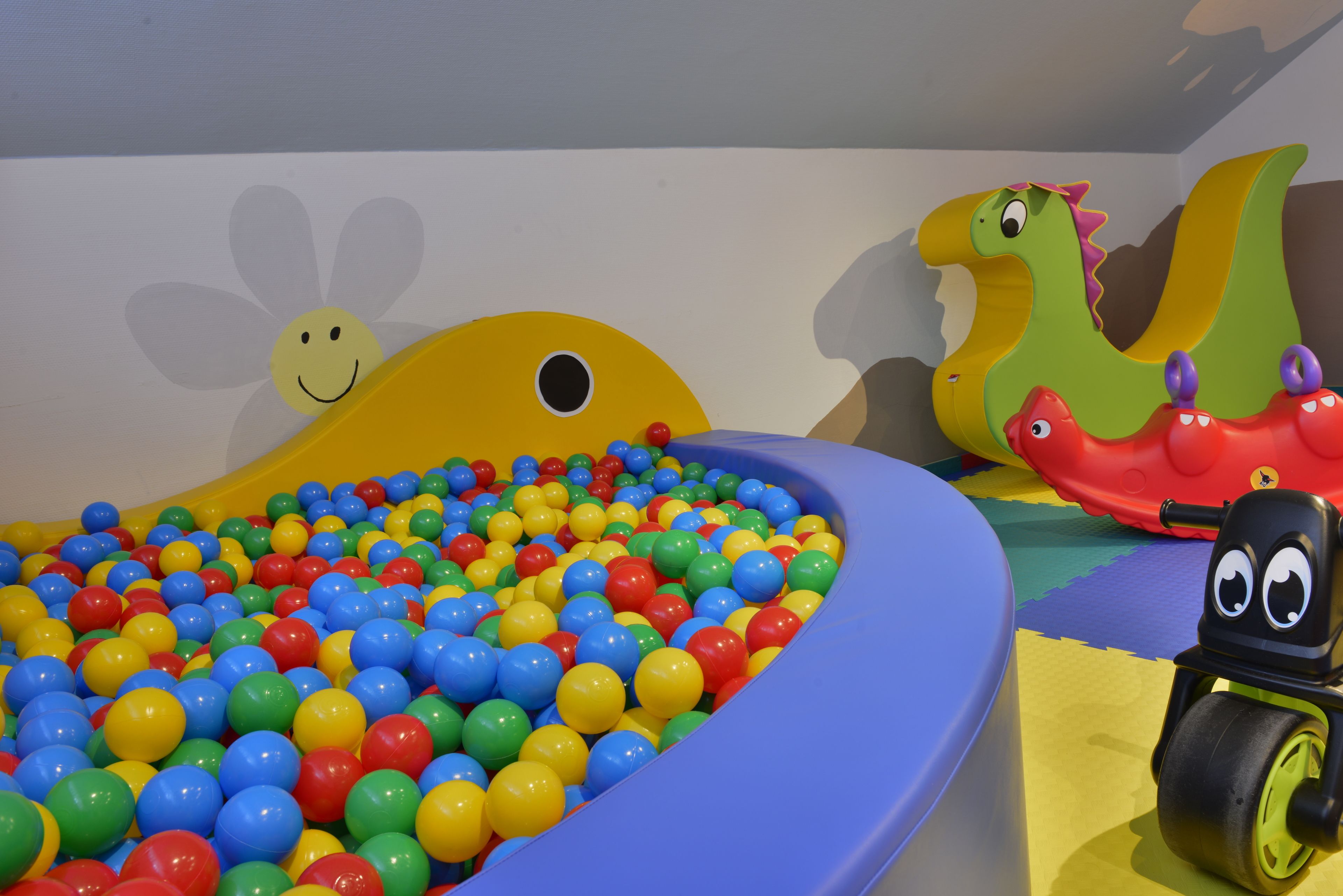 A children's play area with a ball pit, a smiling flower decoration, and a toy dinosaur.