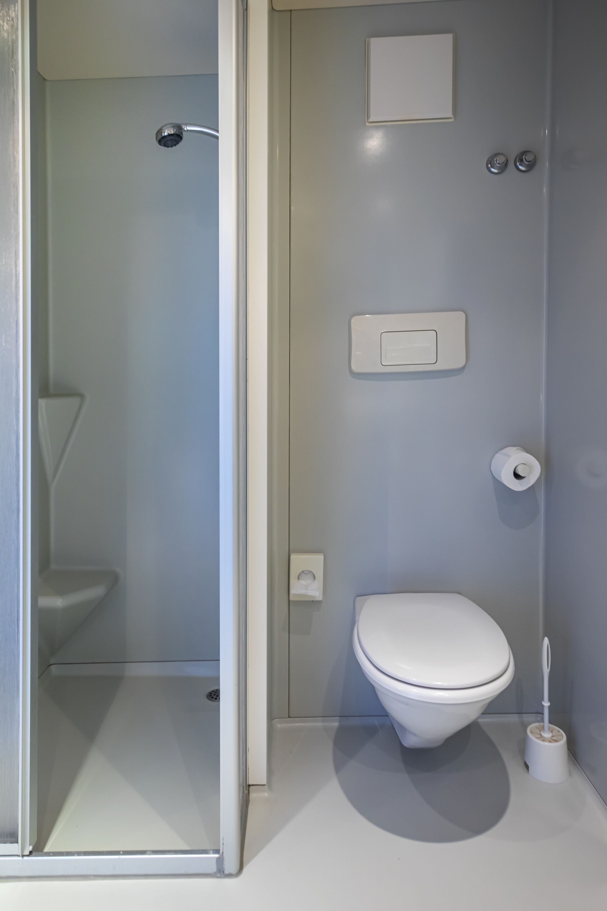 Uma casa de banho moderna com sanita, chuveiro e suporte para papel higiénico.