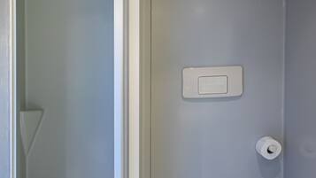 Uma casa de banho moderna com sanita, chuveiro e suporte para papel higiénico.