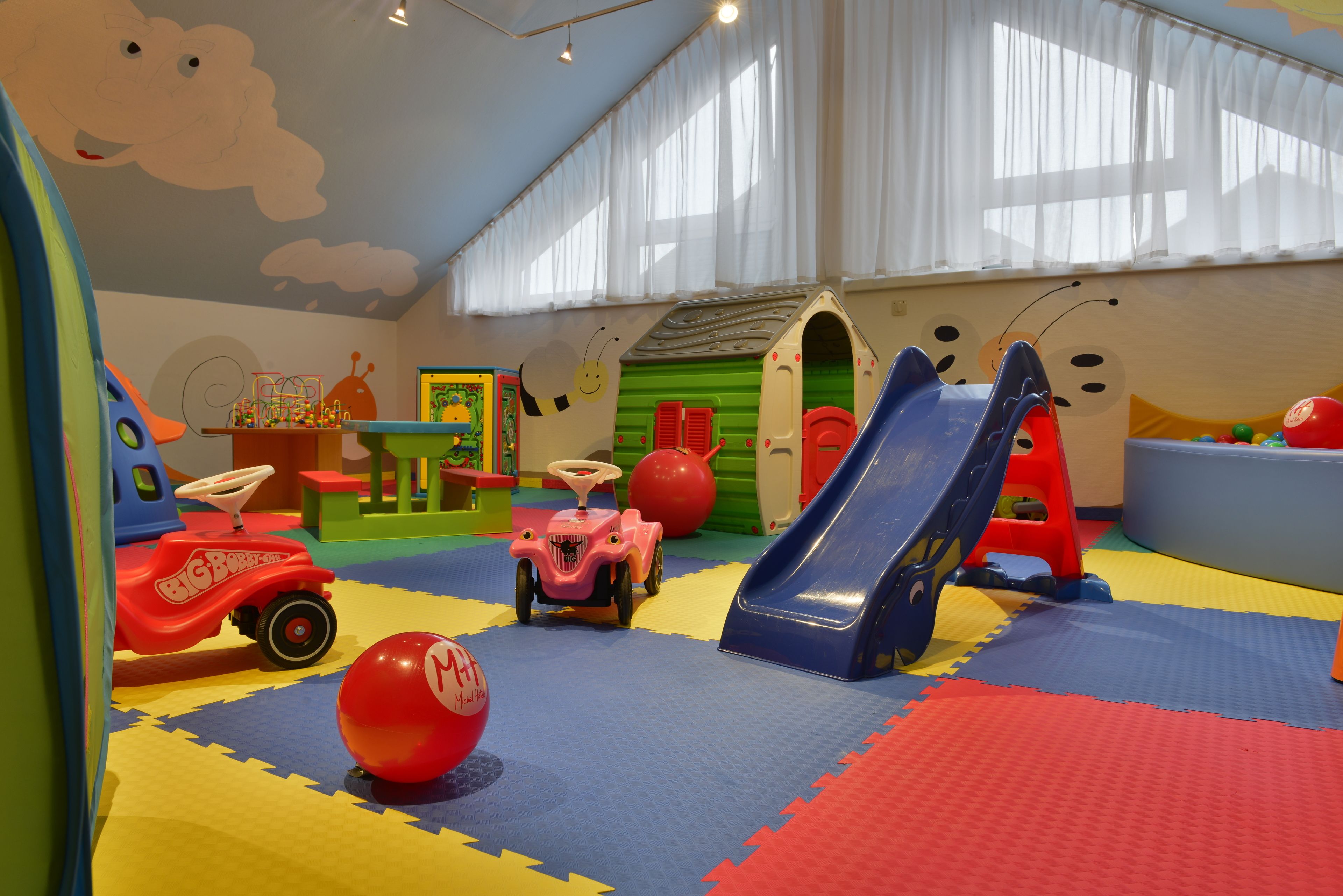 A play area with a slide, a small car, and colorful play mats.