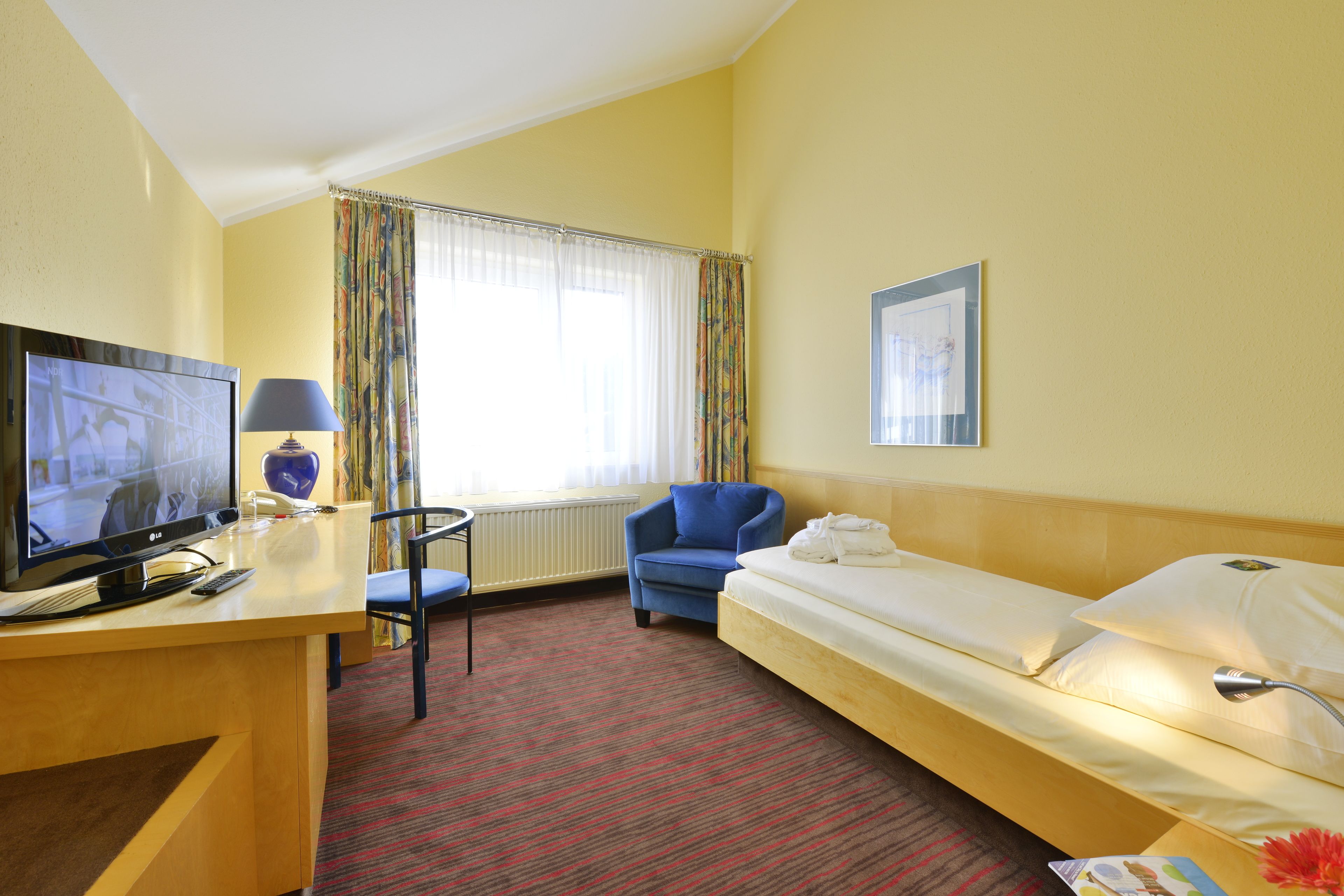 A hotel room with a bed, a desk with a television, a chair, and a window with curtains.