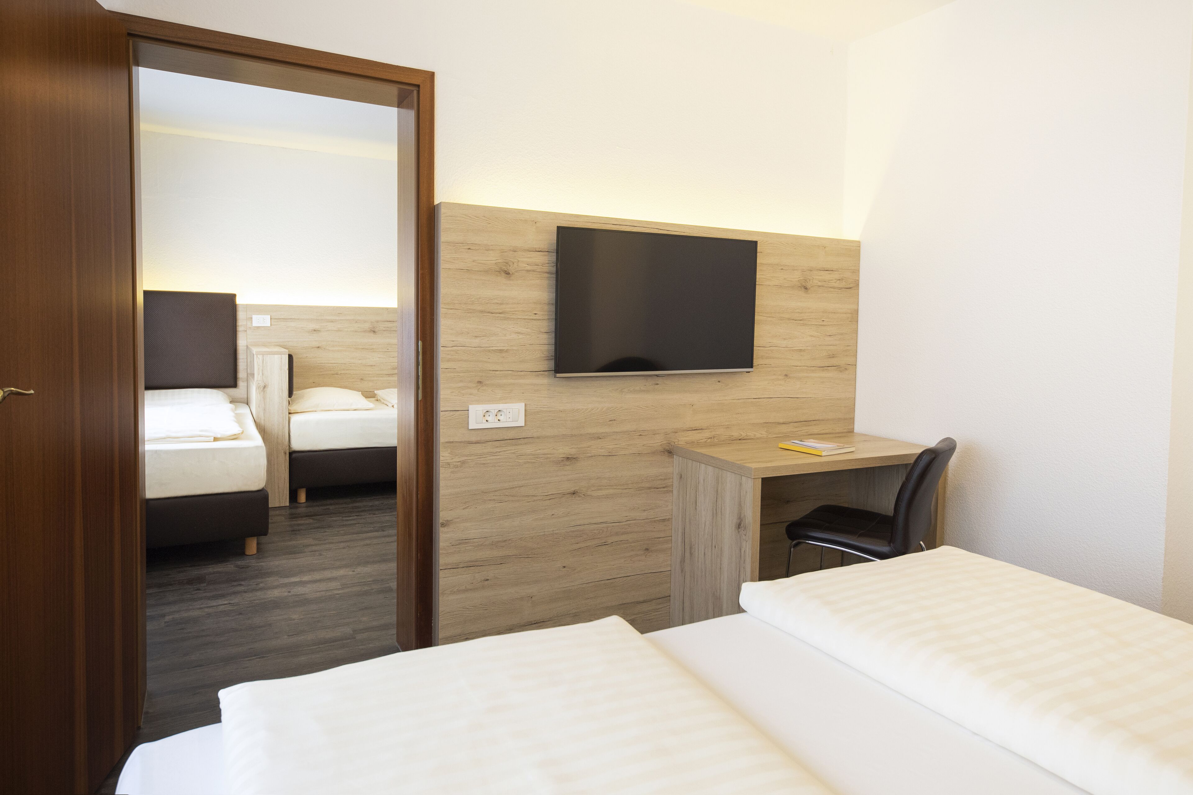 A hotel room with a bed, a desk, a chair, and a TV mounted on the wall.