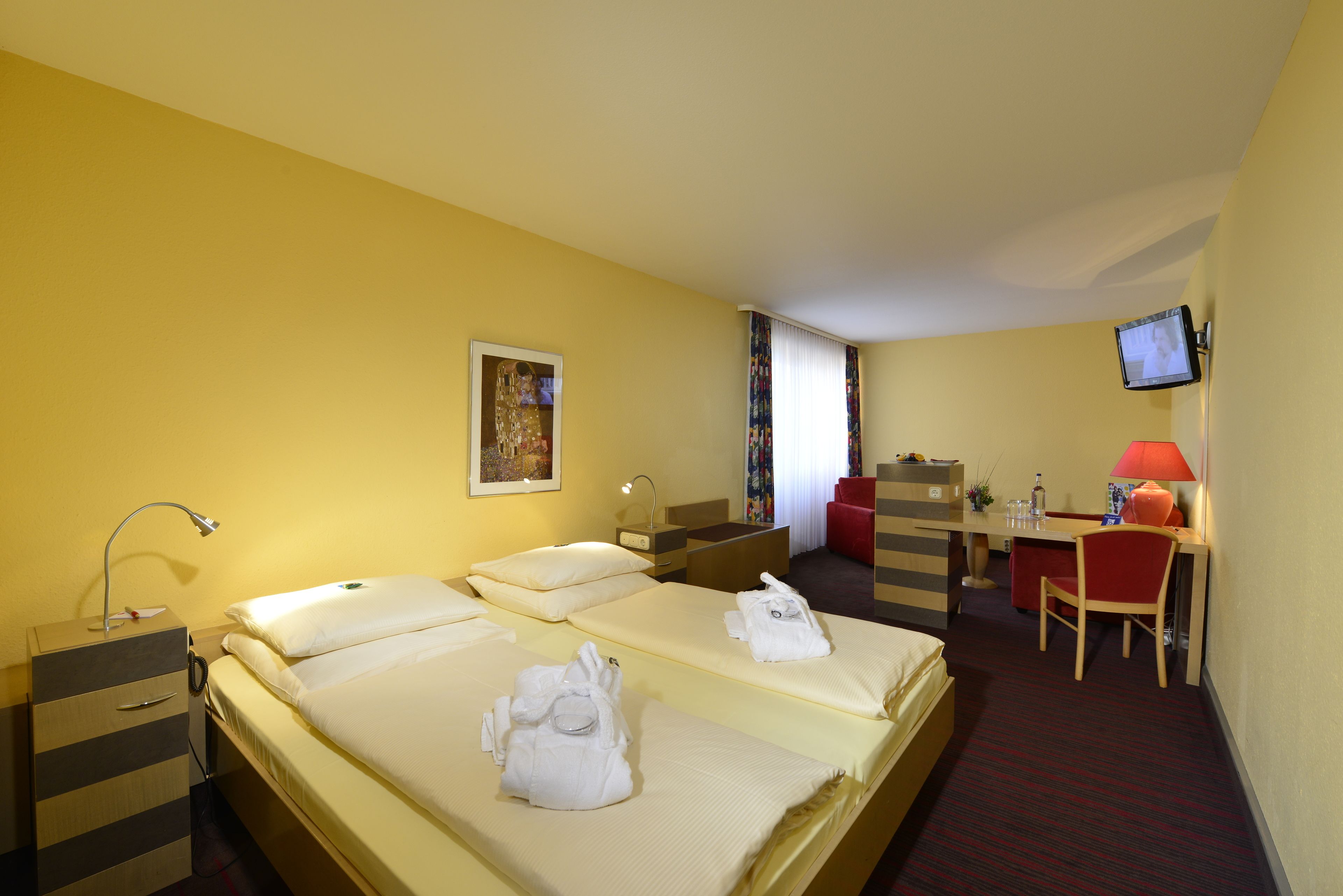 A hotel room with two beds, a desk, a chair, a TV, and a bathroom.