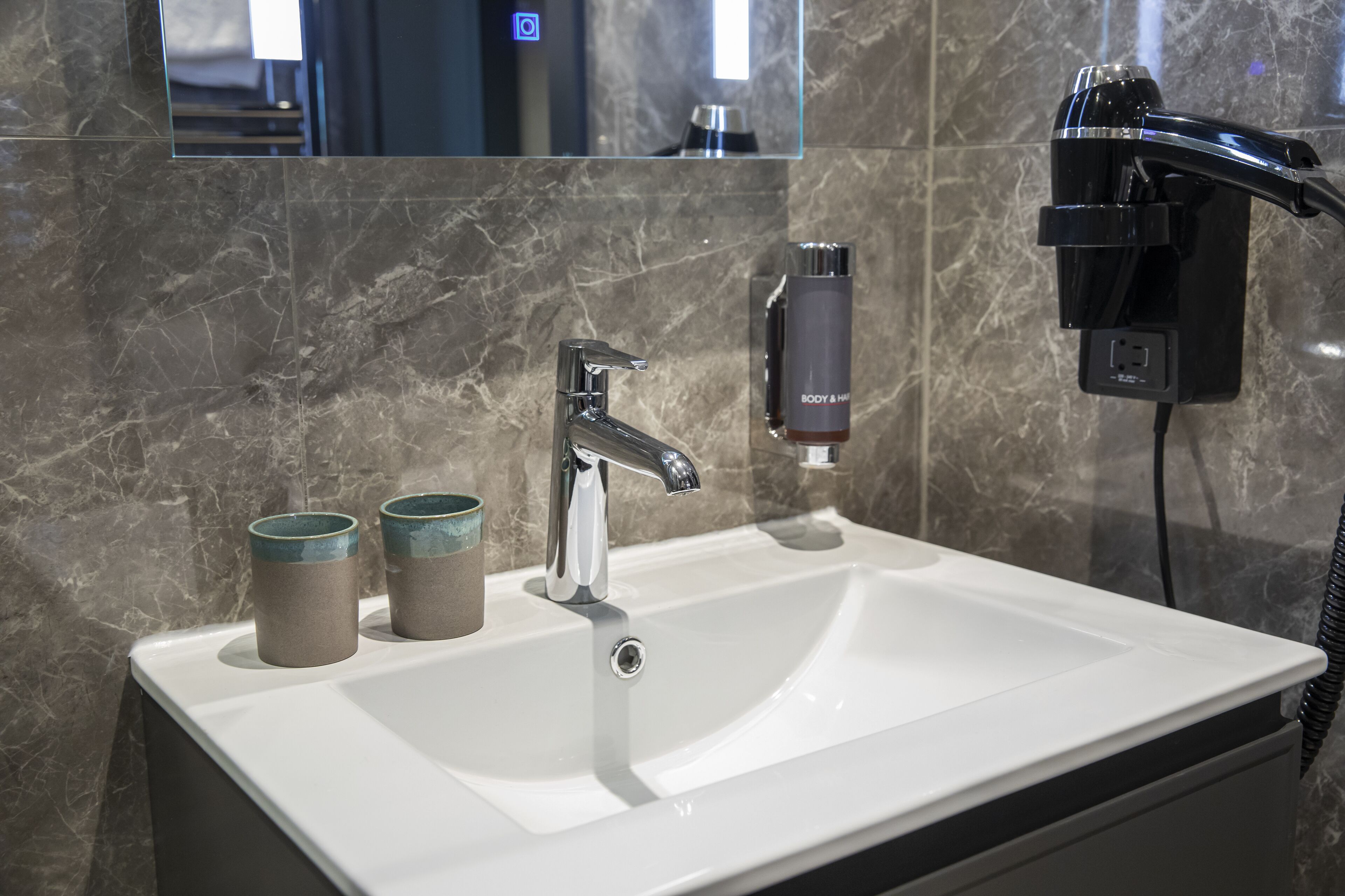 A bathroom with a white sink, a chrome faucet, and a mirror above it. There are two ceramic cups on the sink.