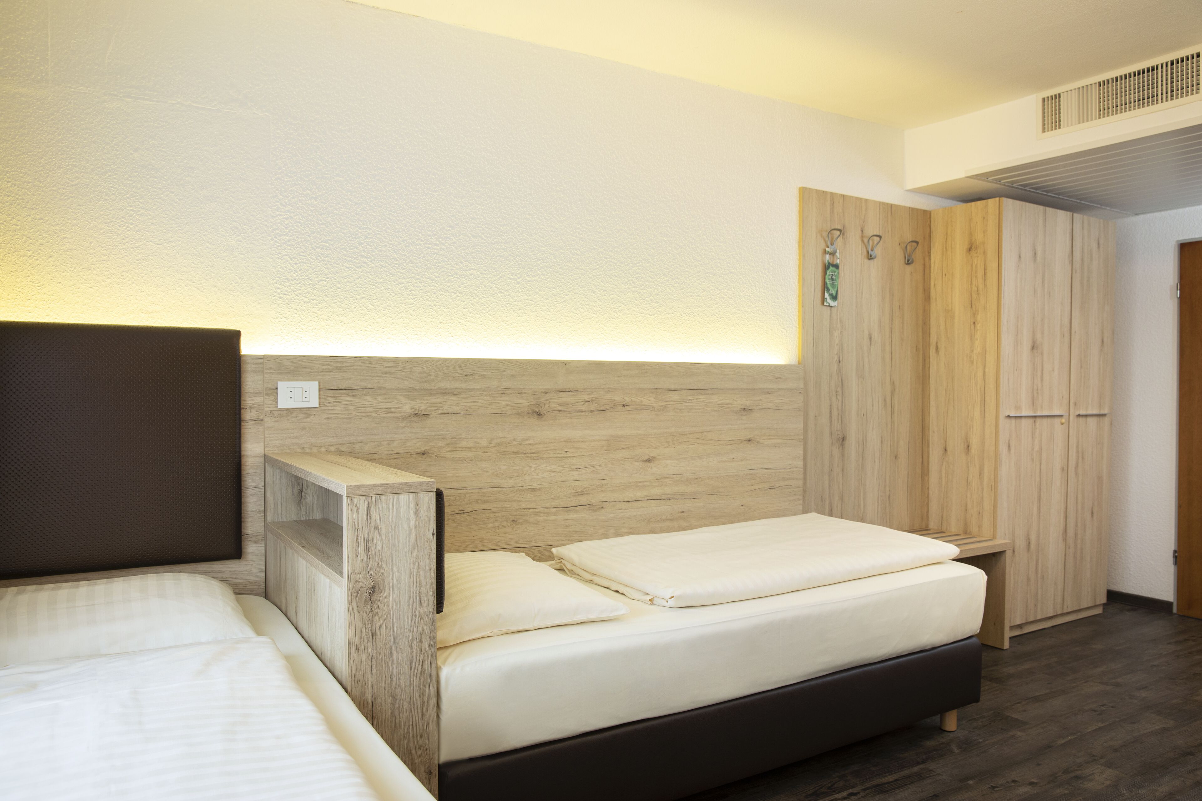 A bedroom with a bed, a wooden headboard, a wardrobe, and a bedside table.