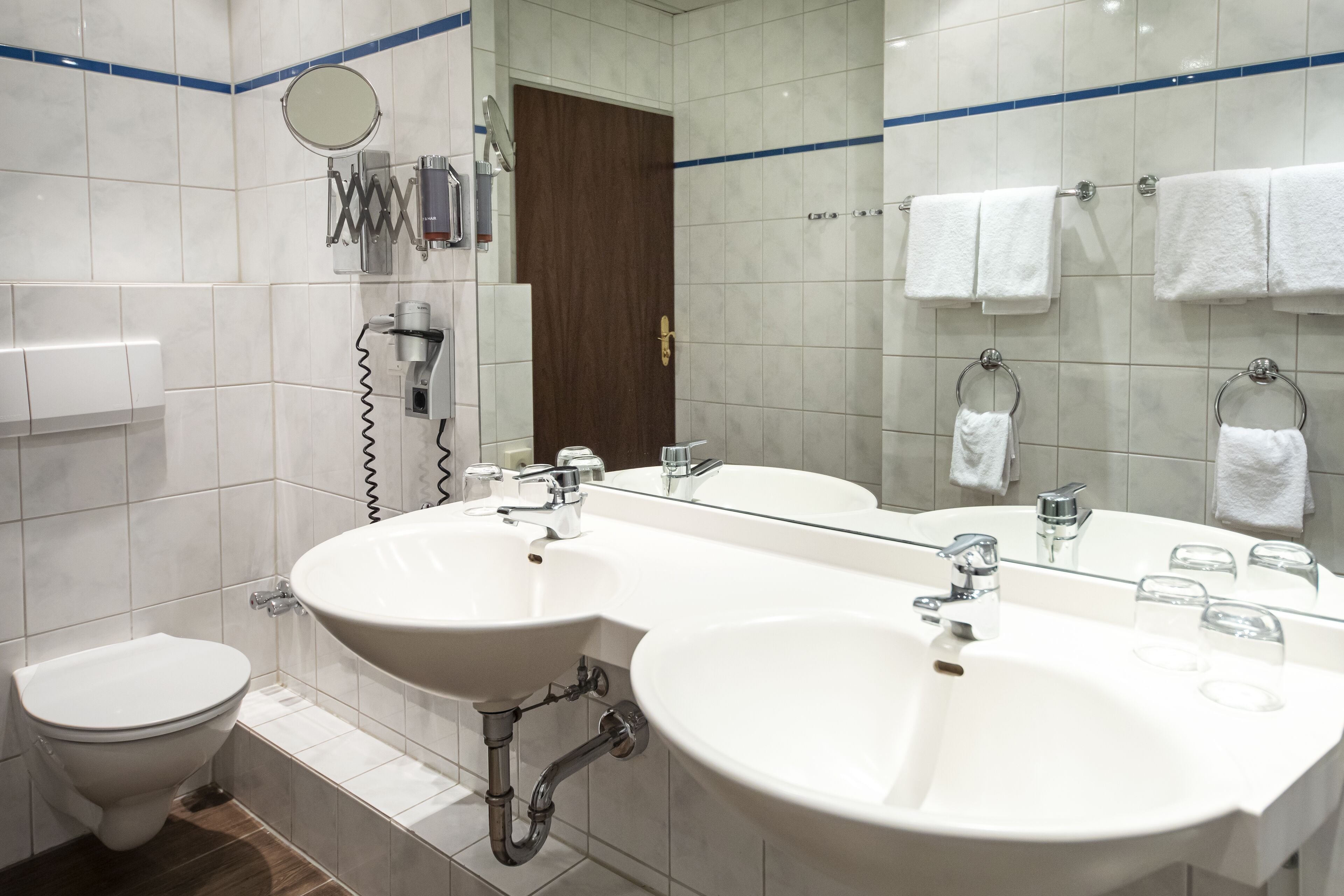 A modern bathroom with two sinks, a toilet, a mirror, and a towel rack.