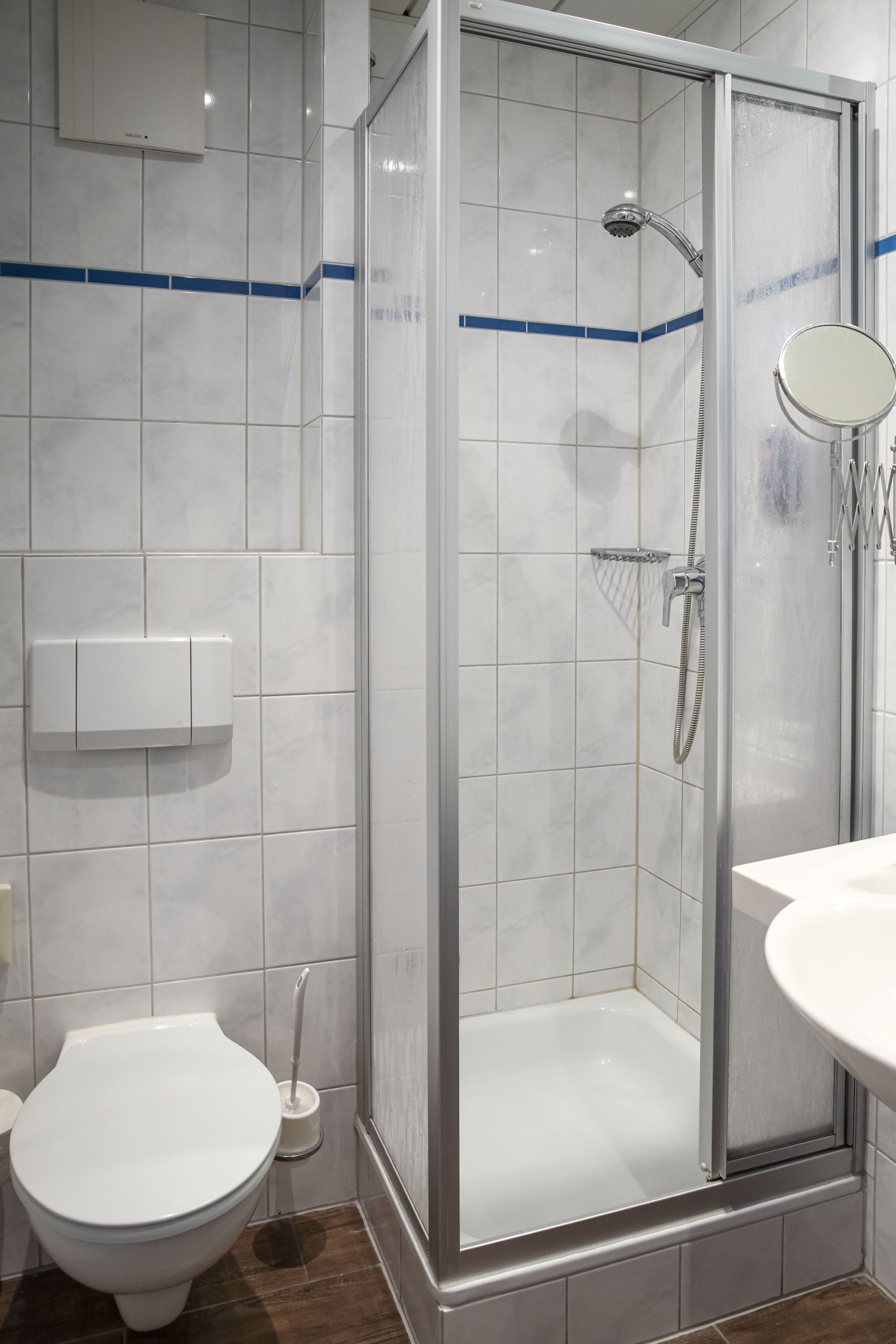 Moderni kylpyhuone, jossa on lasiseinällä varustettu suihku, wc ja peilillä varustettu pesuallas.