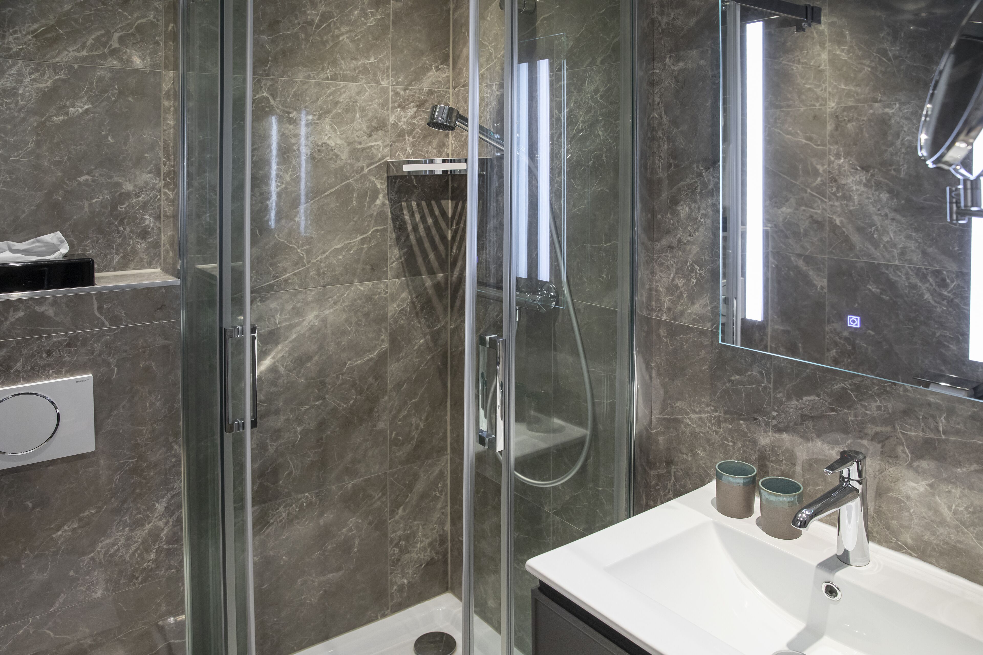 Un baño moderno con ducha de vidrio, lavamanos blanco y un espejo grande.