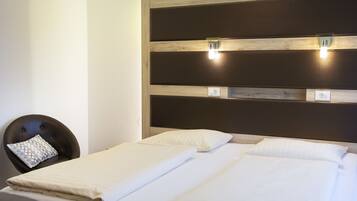 Ein Hotelzimmer mit zwei Betten, einem Bettkopfteil mit integrierter Beleuchtung, einem Sessel mit einem gemusterten Kissen und einer wandmontierten Leuchte.