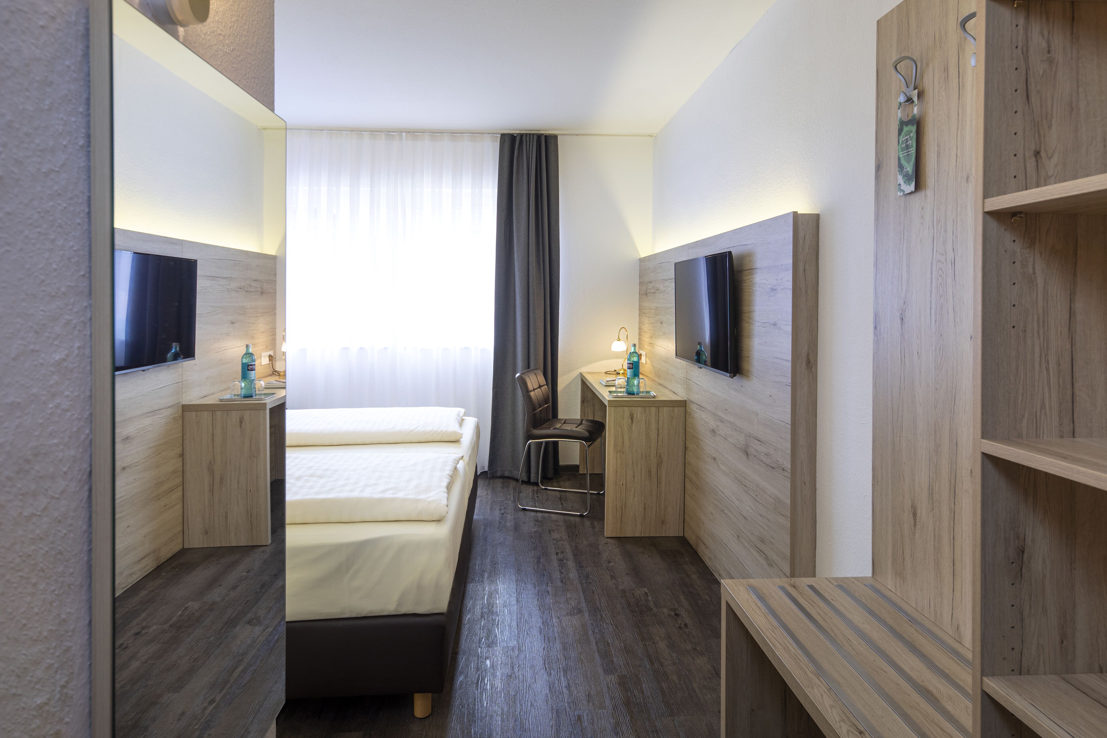 Une chambre d’hôtel avec un lit, un bureau, une chaise, une télévision et un miroir.