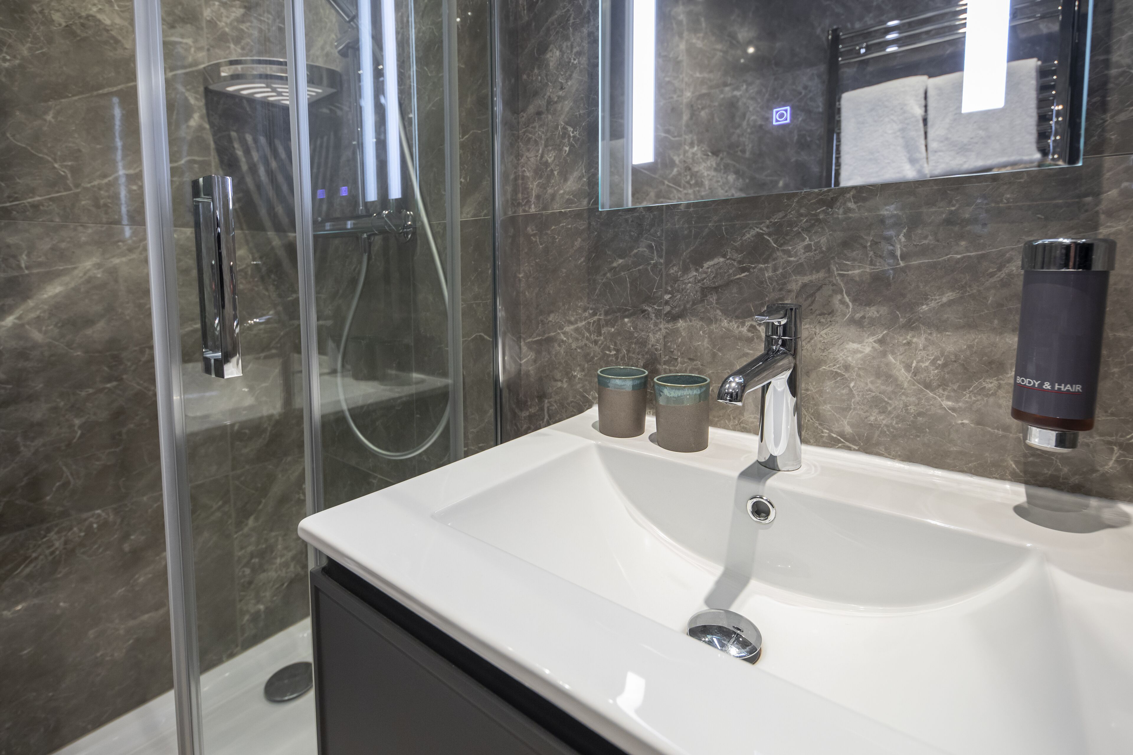 Een moderne badkamer met een douchecabine van glas, een wit wastafeltje en een spiegel erboven.
