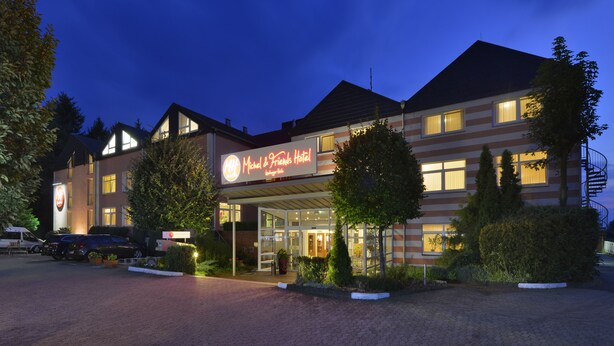 A hotel with a modern design, featuring a prominent sign, a covered entrance, and a parking area. - Hotel am Park Lüneburger Heide (Hodenhagen)