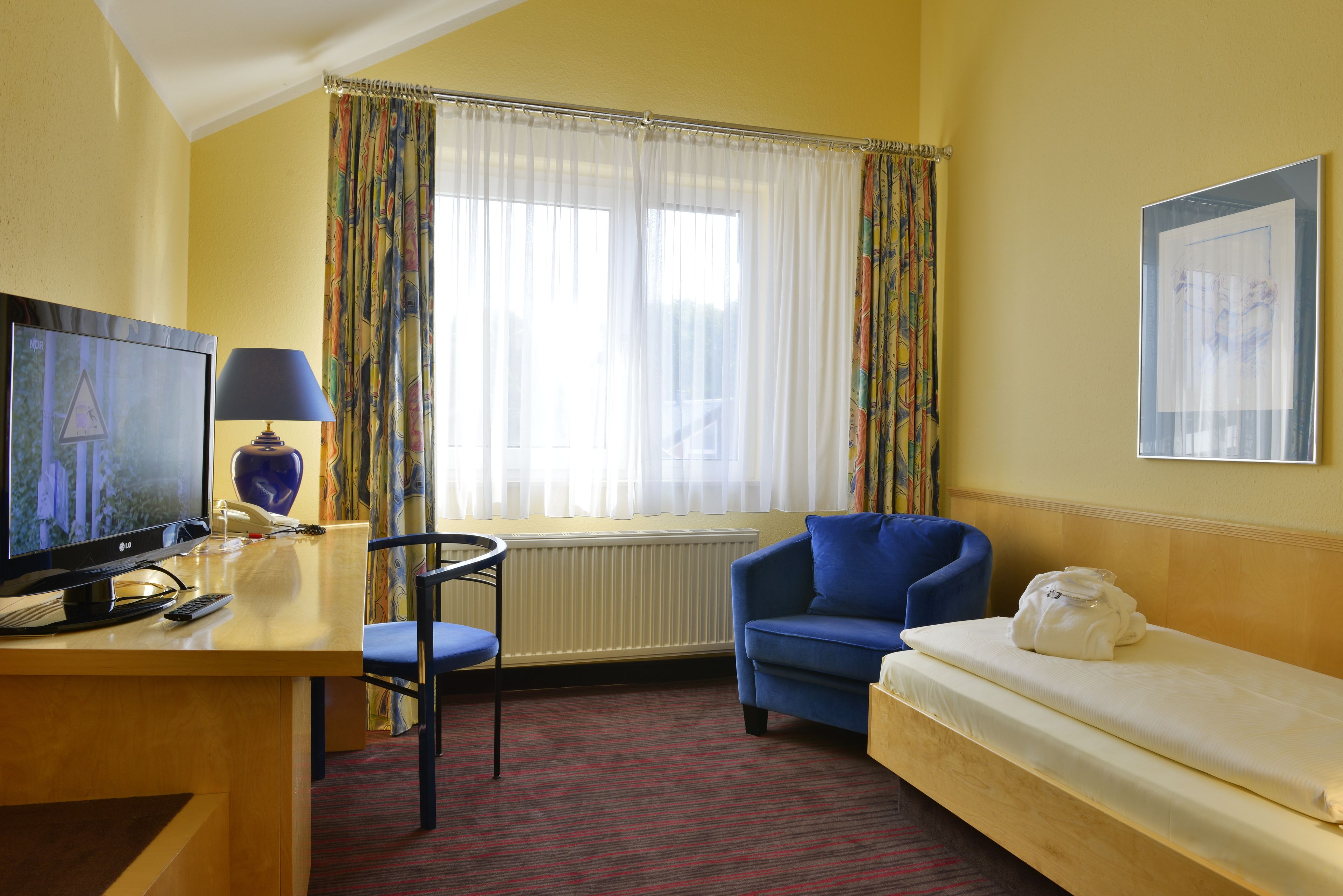 Une chambre d’hôtel avec un lit, un bureau équipé d’un ordinateur et d’une lampe, une chaise et une fenêtre avec des rideaux.