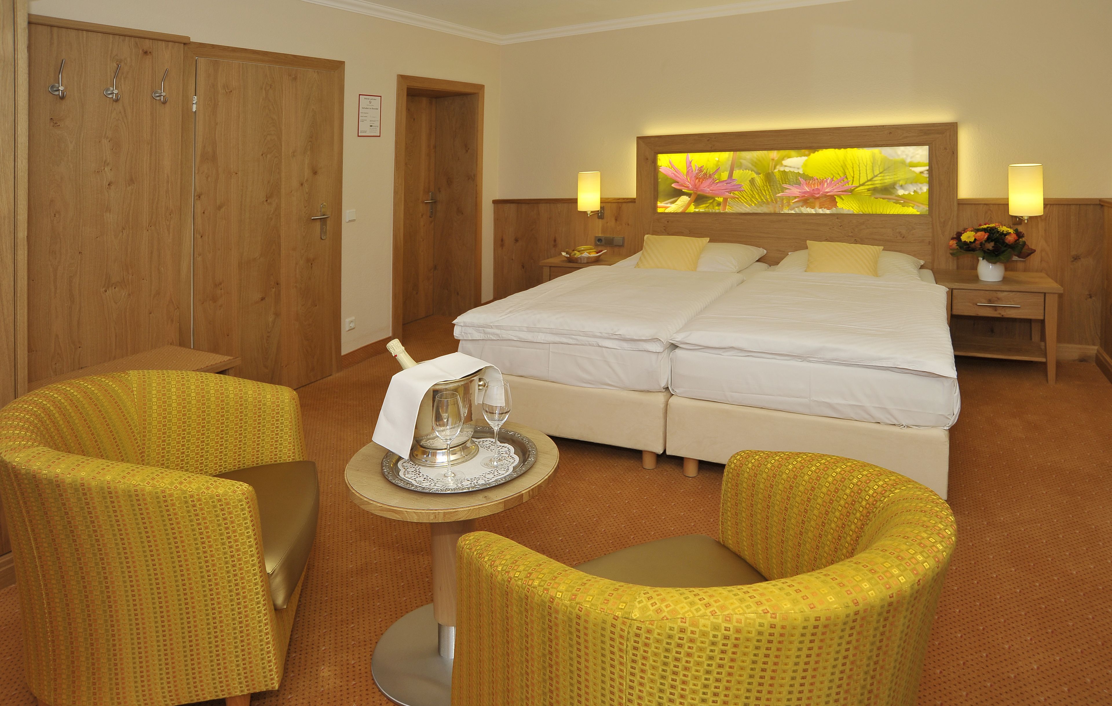 A hotel room with a large bed, two chairs, a small table with a tray, and a nightstand with a lamp.