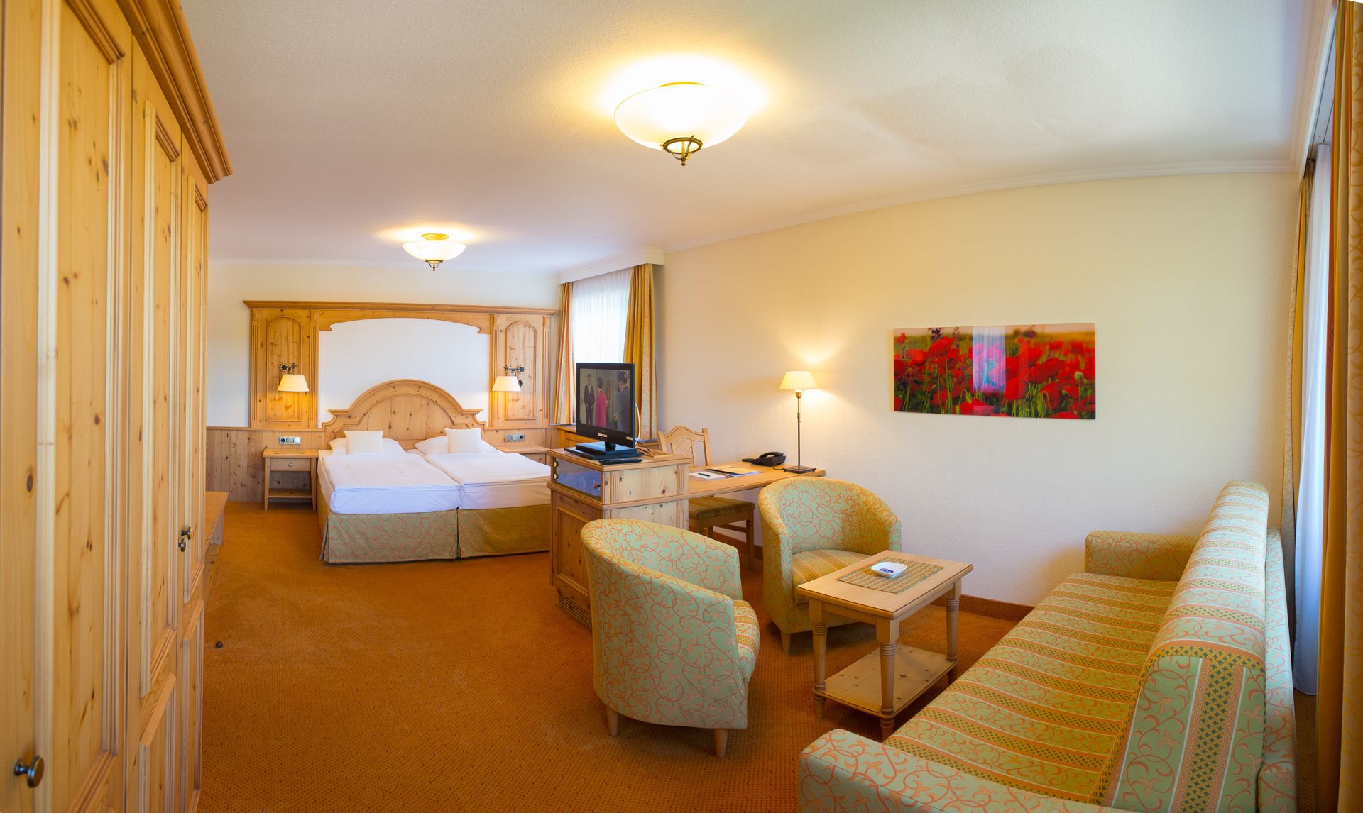 A hotel room with a double bed, a desk with a computer, a TV, two chairs, a small table, and a painting on the wall.
