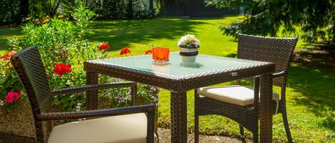 Une table en osier avec deux chaises, un verre et une petite plante en pot, le tout dans un jardin.