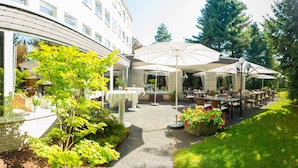 An outdoor patio area with tables and umbrellas, surrounded by greenery and trees. - Gronauer Tannenhof (Bergisch Gladbach)