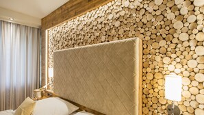 A hotel room with a large bed, a headboard with a quilted design, and a wall decorated with stacked logs. - Gronauer Tannenhof (Bergisch Gladbach)