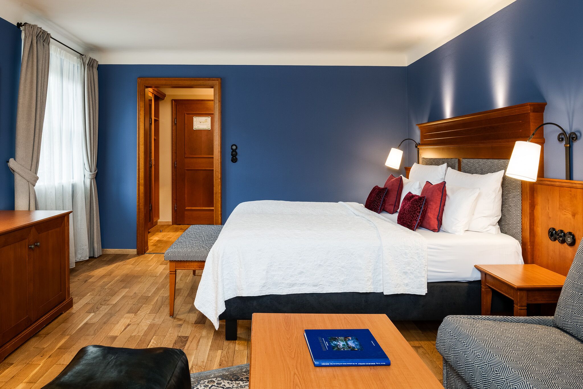A hotel room with a large bed, two bedside lamps, a wooden nightstand, a desk, and a chair.
