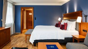 A hotel room with a large bed, two bedside lamps, a wooden nightstand, a desk, and a chair.