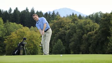 A golf course with a golfer preparing to hit a ball, a golf bag, and a caddy cart.