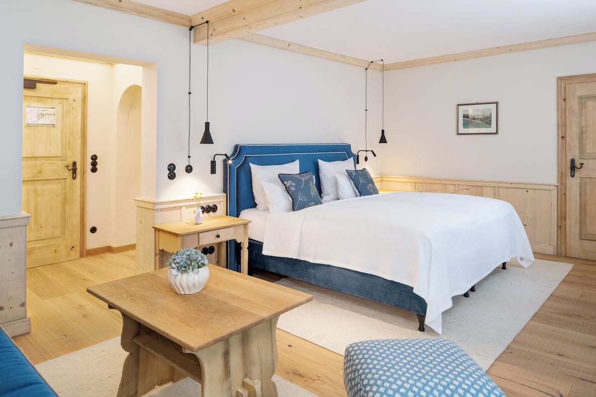 Un dormitorio con una cama de madera, una mesita de noche, una mesa de madera y una silla azul estampada.