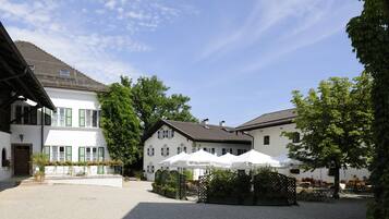 Ein Innenhof mit einem weißen Gebäude, Sitzgelegenheiten im Freien und Sonnenschirmen.
