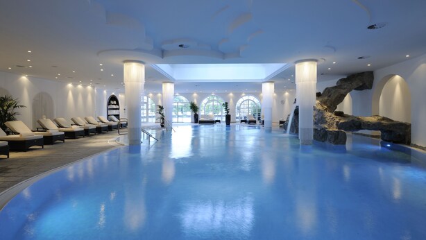 Une piscine intérieure spacieuse, dotée de chaises longues et d’un espace de détente central.