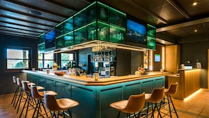 Un espace bar doté d’un îlot central, de tabourets de bar et d’un grand panneau lumineux placé au-dessus.