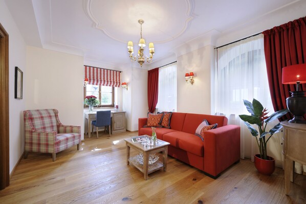 A living room with a red sofa, a plaid armchair, a wooden coffee table, and a chandelier.