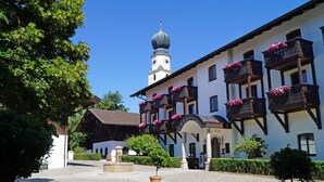 Un bâtiment traditionnel doté d’une tour horlogée, d’une cour avec une fontaine et de jardinières fleuries sur les balcons.