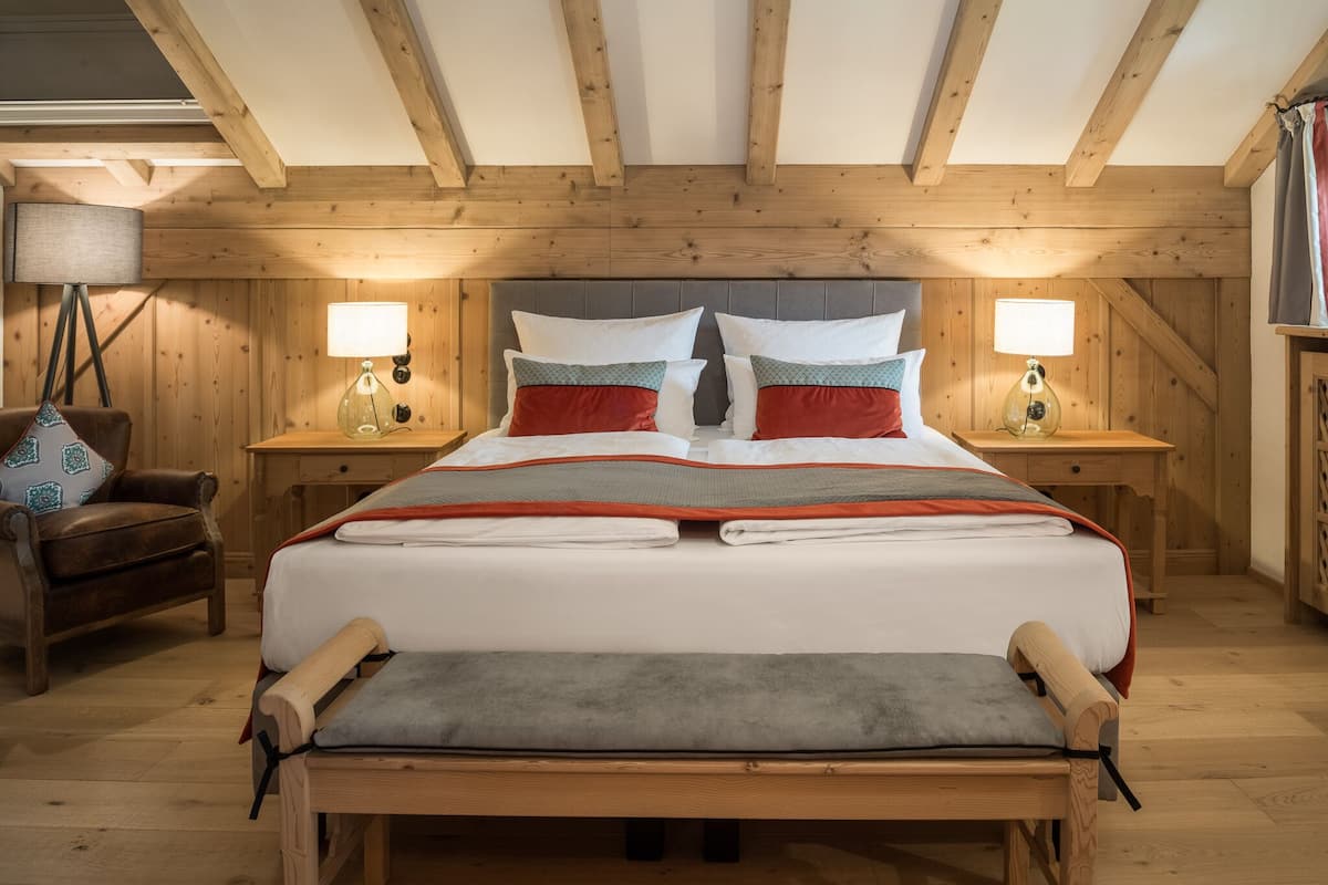 Un dormitorio con paneles de madera, una cama grande, dos mesitas de noche con lámparas, una silla y un banco.