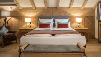 Un dormitorio con paneles de madera, una cama grande, dos mesitas de noche con lámparas, una silla y un banco.