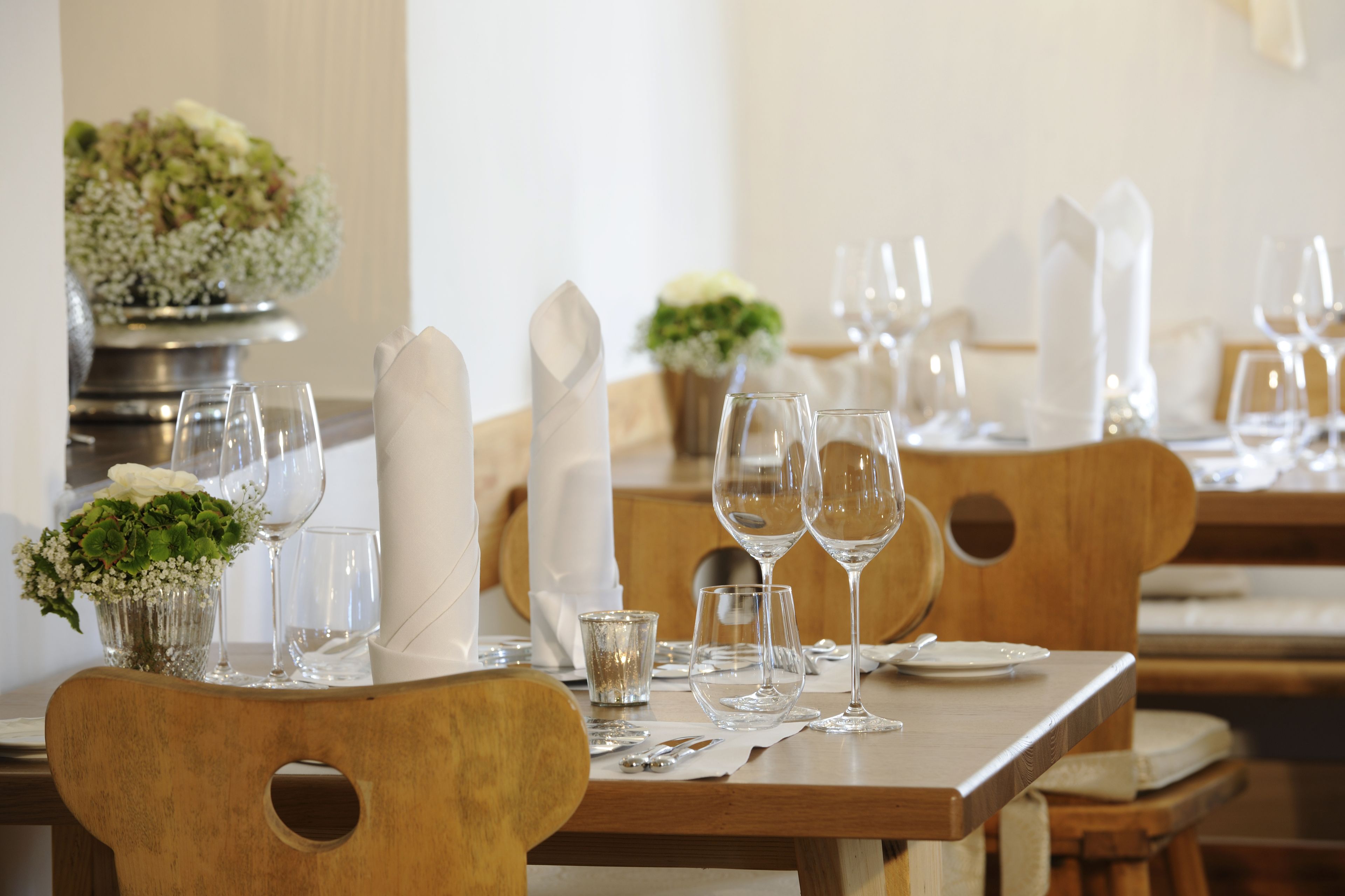 Une table à manger dressée avec des serviettes blanches, des verres transparents et un petit vase rempli de fleurs.