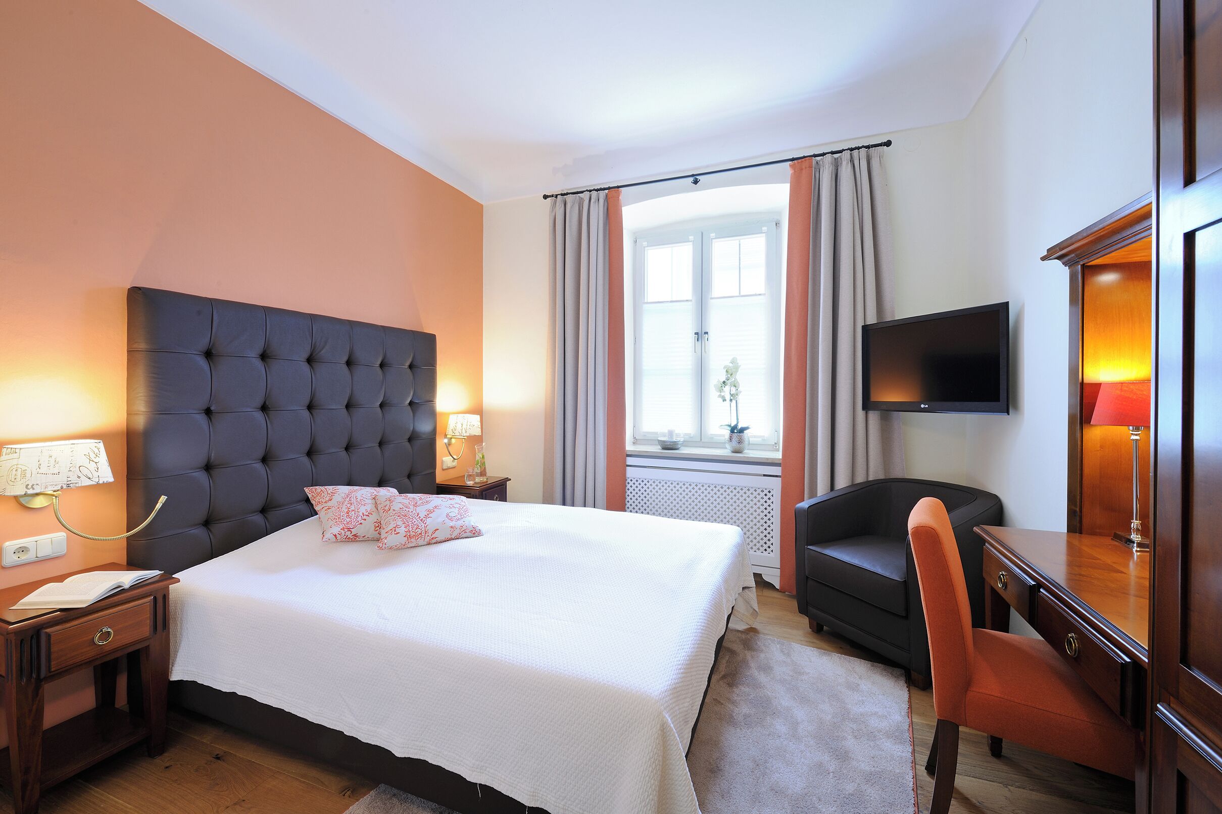Habitación de hotel con una cama grande, un escritorio, una silla, un televisor y una ventana con cortinas.