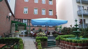 An outdoor patio area with tables and chairs, a blue umbrella, and a fountain. - Hotel Elefant (Schwerin)