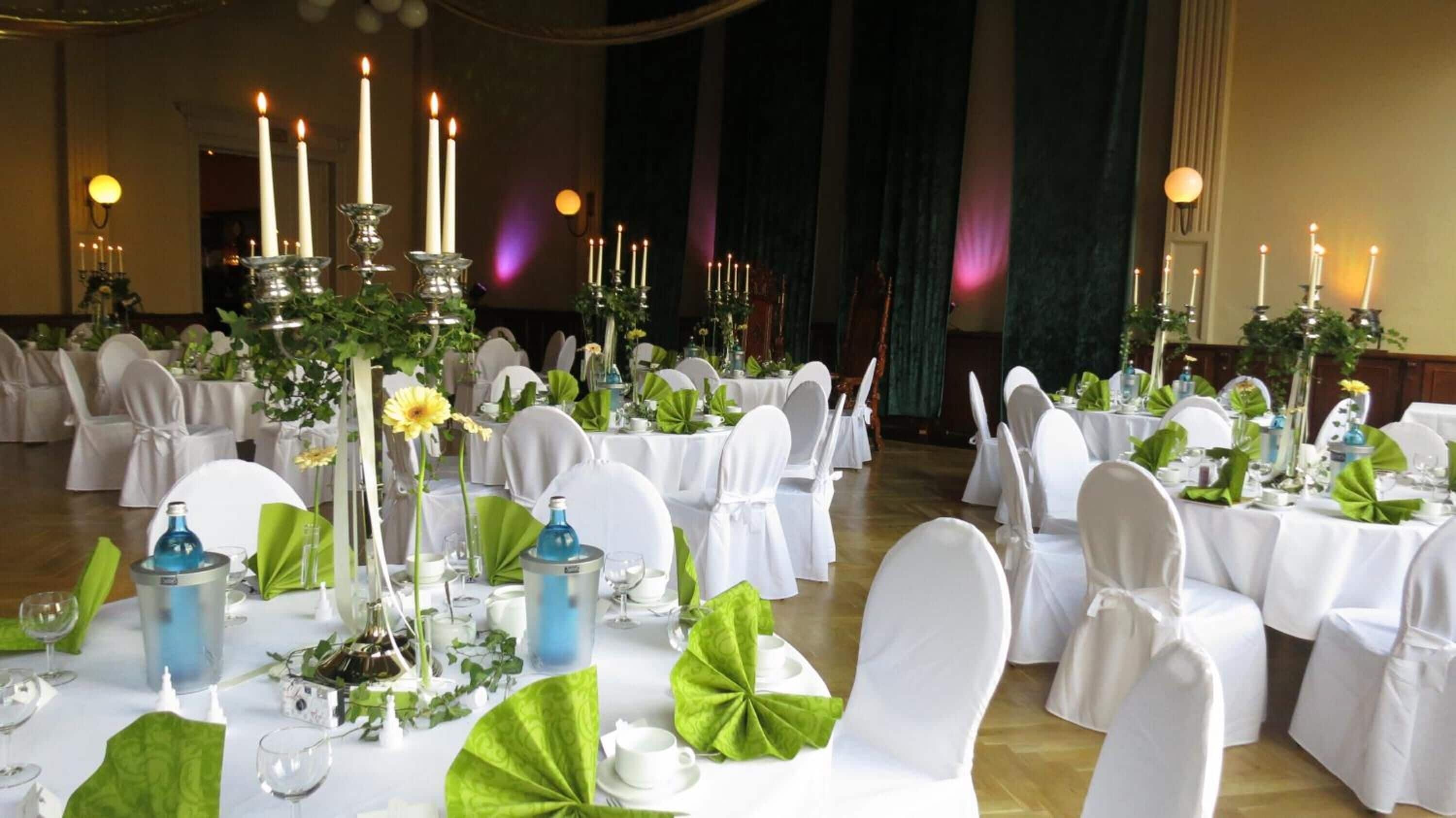 A banquet hall with round tables set for a formal event, each with white tablecloths, green centerpieces, and white chairs.