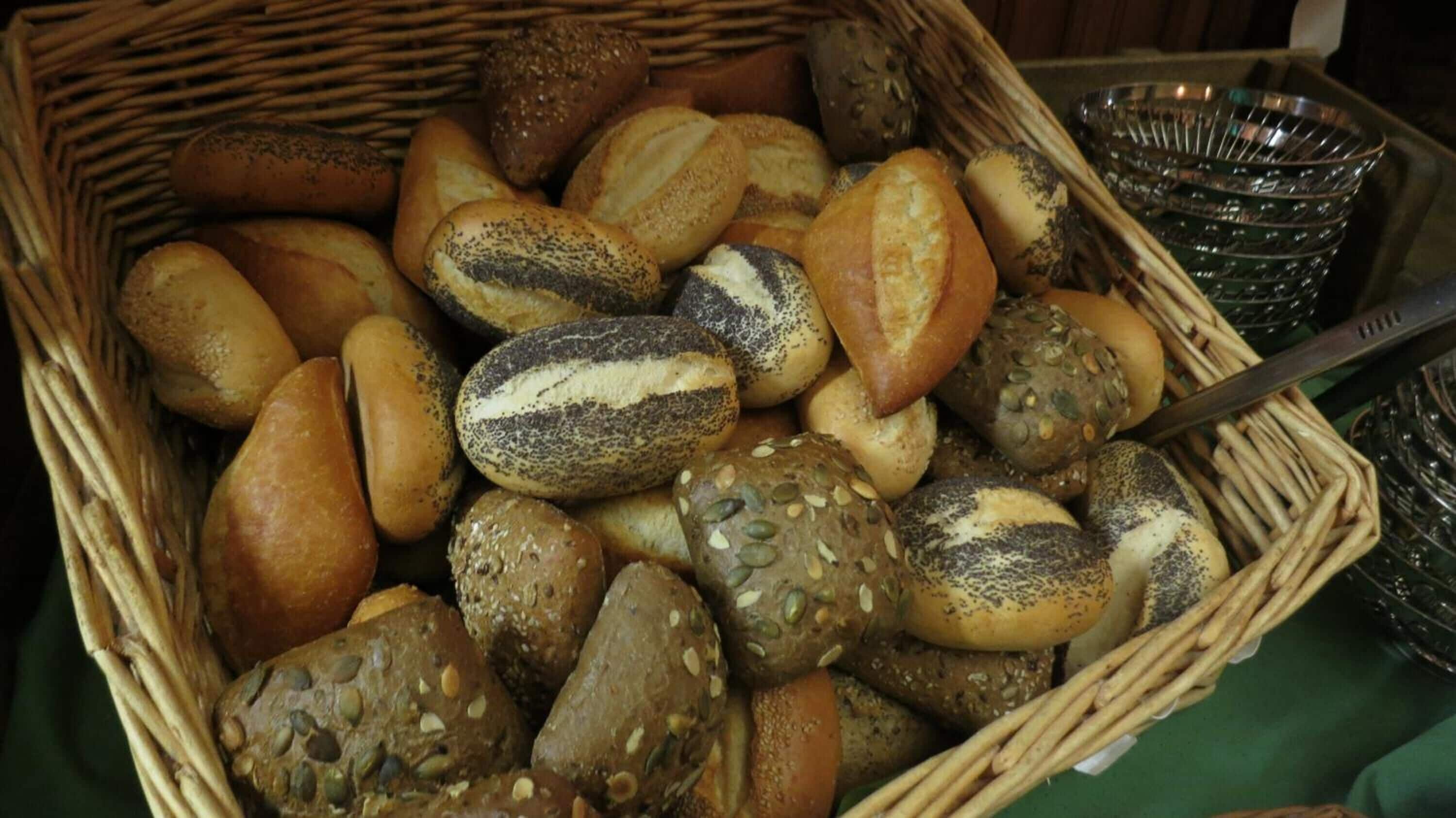A wicker basket filled with various types of bread, including seeded and poppy-seeded varieties.