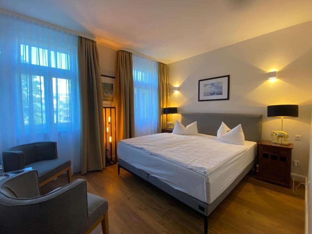 Una habitación de hotel con una cama, mesitas de noche, una silla y cortinas.