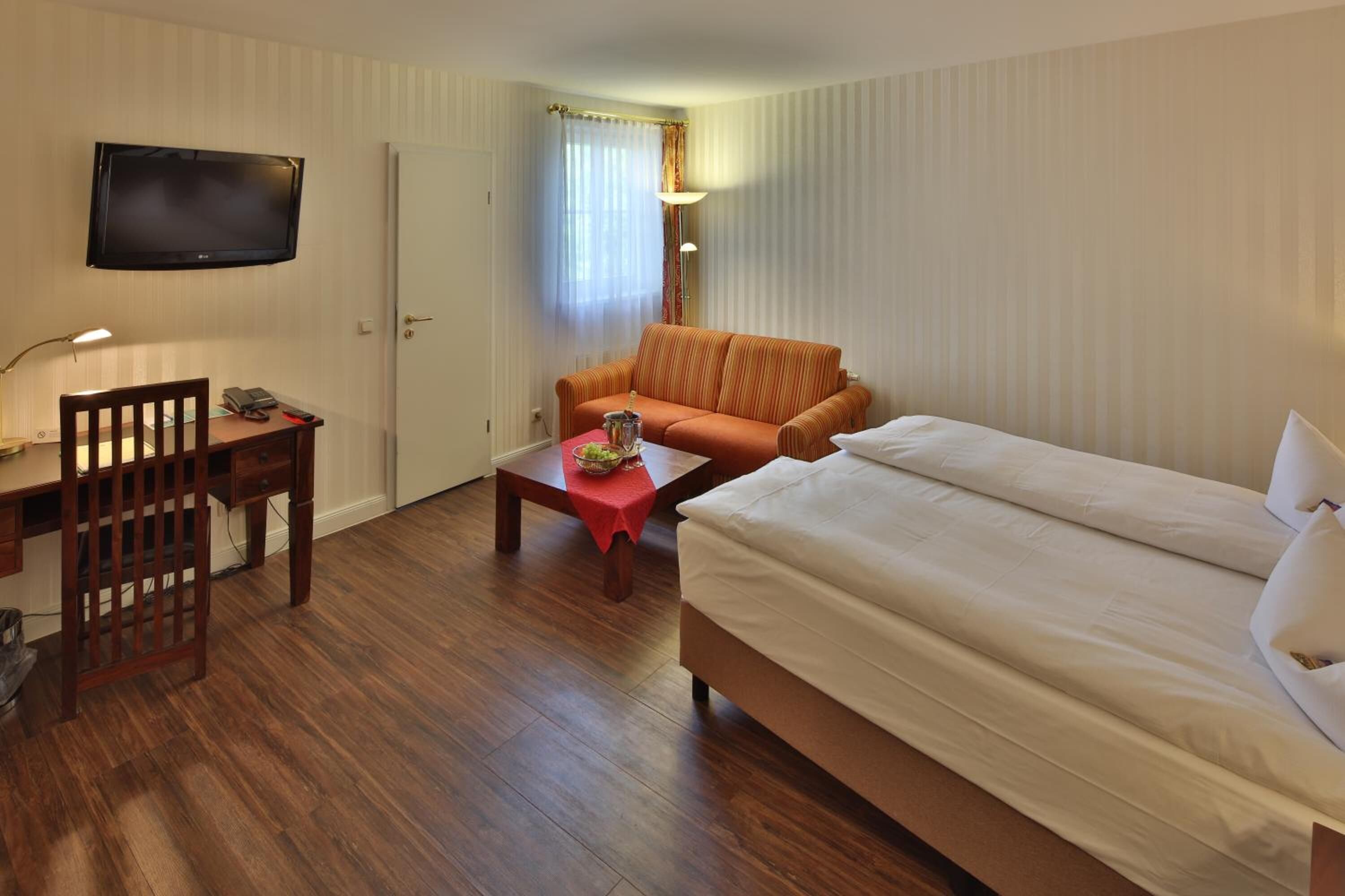 A hotel room with a bed, a desk with a chair, a television, and a sofa.