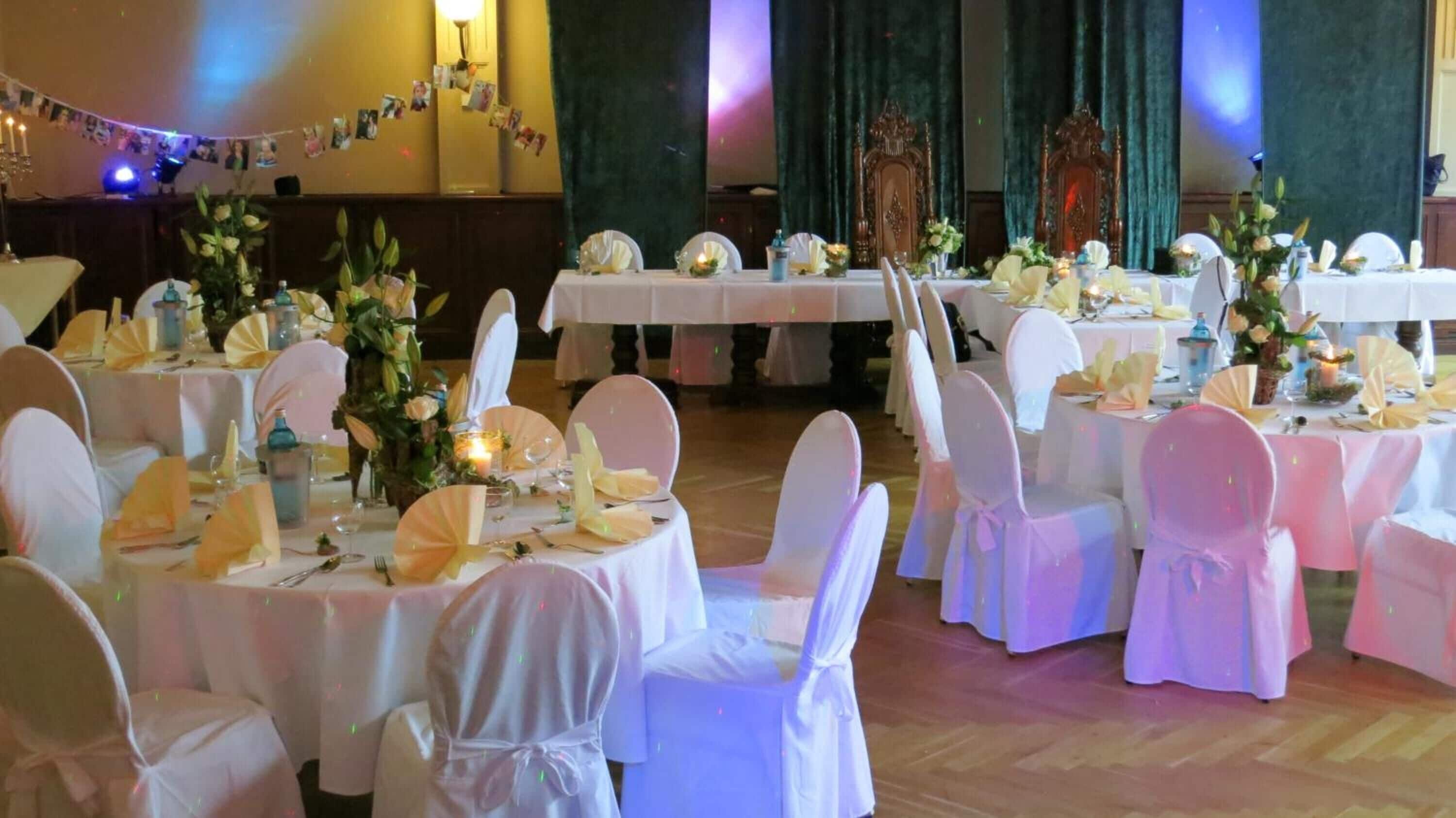 Un salón de banquetes con mesas redondas, manteles blancos y sillas cubiertas de blanco.