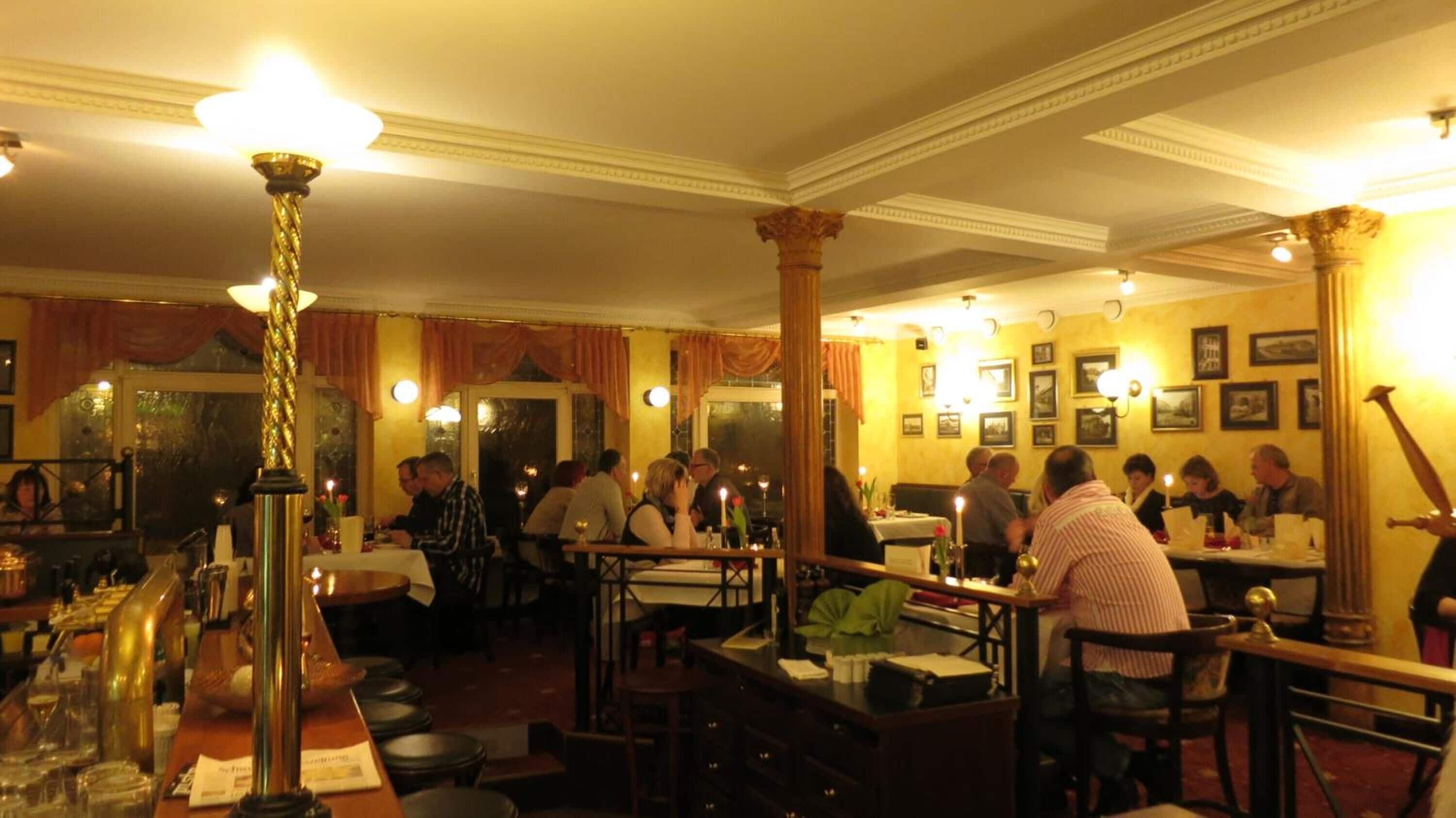 A restaurant with multiple tables and chairs, a bar area with stools, and a warm, dimly lit ambiance.