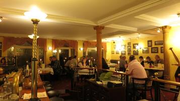 A restaurant with multiple tables and chairs, a bar area with stools, and a warm, dimly lit ambiance.