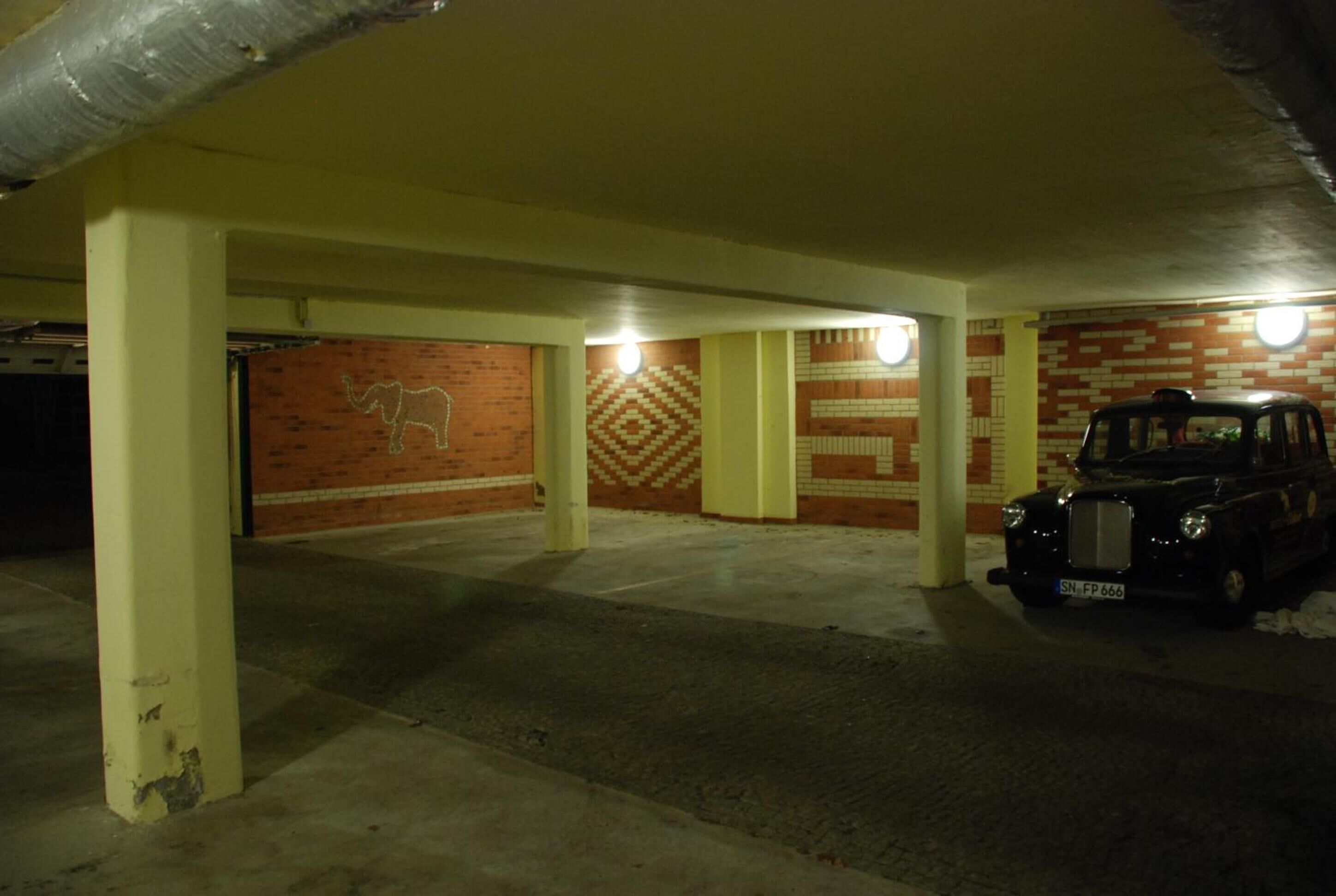 Uma garagem subterrânea com paredes de tijolo e pilares de concreto, um carro estacionado em uma das vagas.