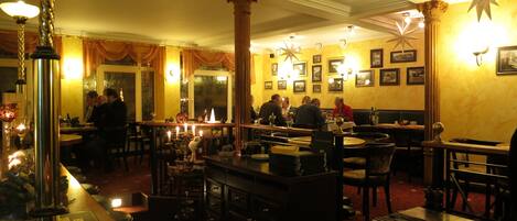 Un restaurante con varias mesas y sillas, una zona de bar y un candelabro.