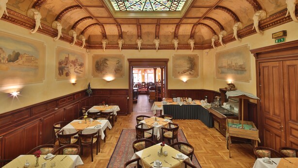 A dining area with wooden tables and chairs, a central aisle, and a stained glass ceiling. - Hotel Elefant (Schwerin)