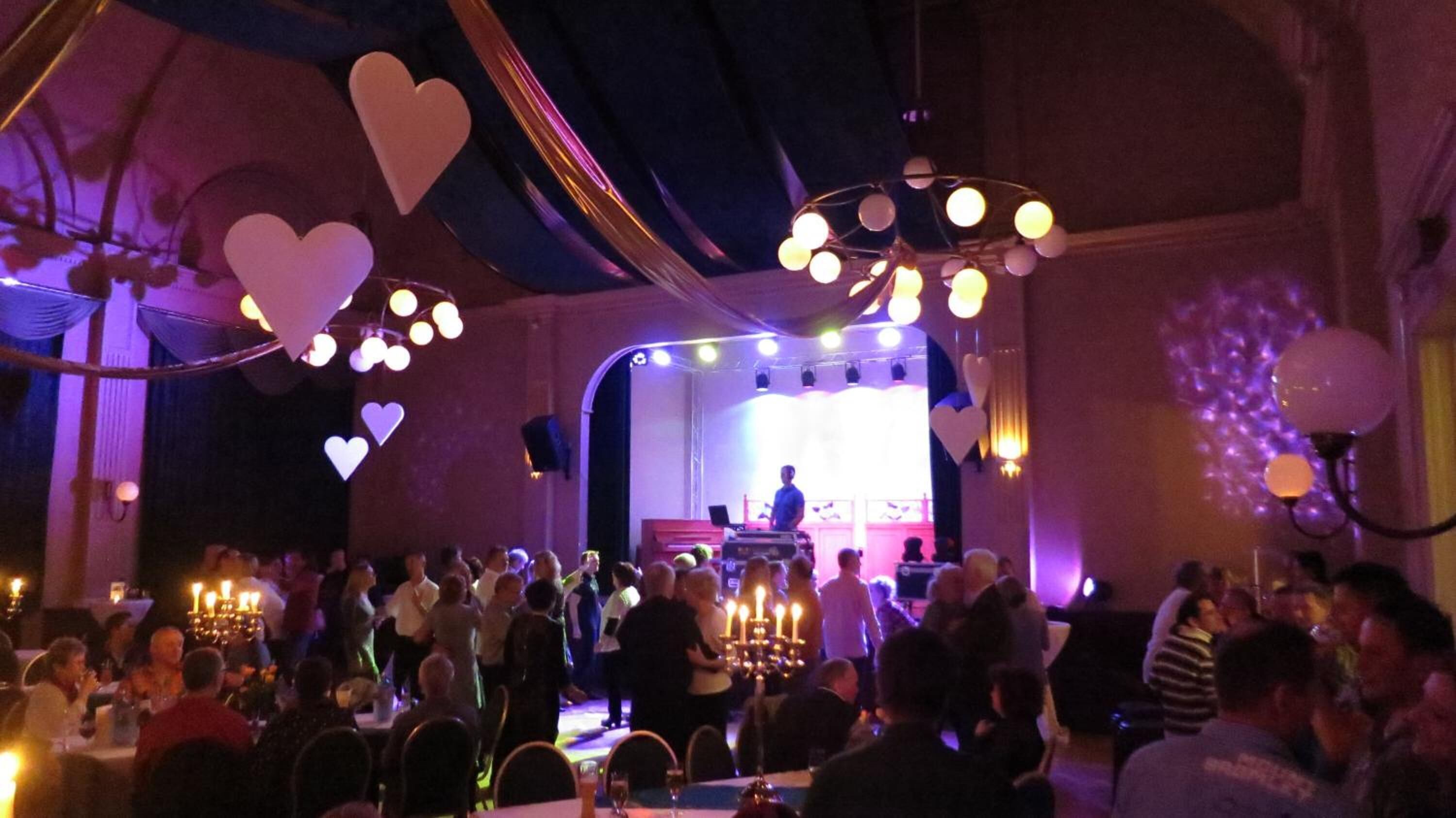 Un salón de baile con escenario, candelabros y decoración con forma de corazón.